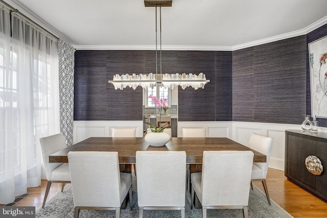 dining area with a wainscoted wall, ornamental molding, visible vents, wallpapered walls, and light wood-style floors