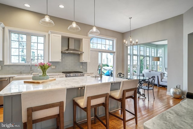 kitchen with wall chimney exhaust hood, a sink, range, decorative backsplash, and light stone countertops