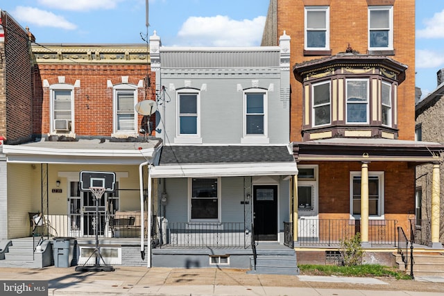 multi unit property with cooling unit, a shingled roof, covered porch, and brick siding