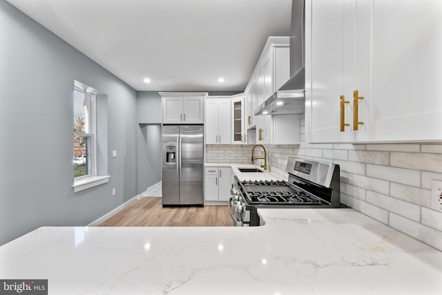 kitchen with a sink, appliances with stainless steel finishes, light stone counters, and wall chimney exhaust hood