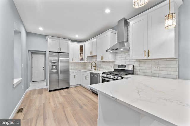kitchen with light stone countertops, stainless steel appliances, tasteful backsplash, white cabinetry, and wall chimney range hood