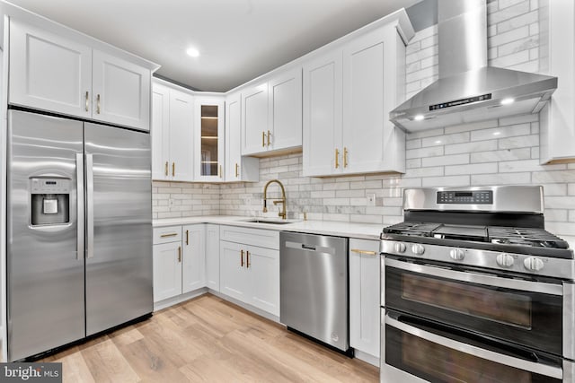 kitchen with light countertops, white cabinetry, appliances with stainless steel finishes, light wood-style flooring, and wall chimney range hood