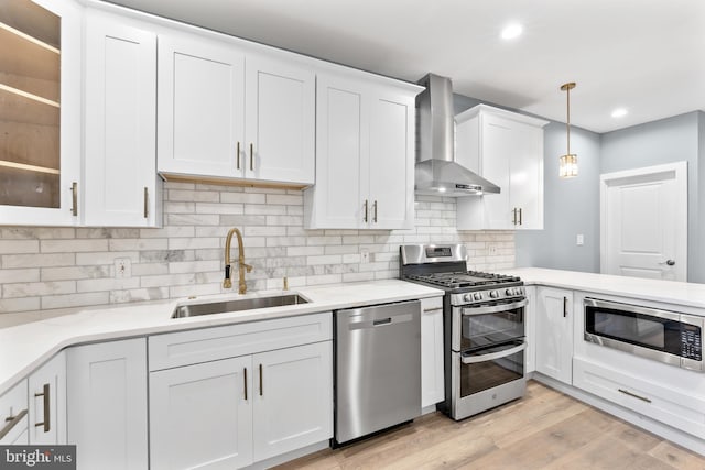kitchen with a sink, white cabinetry, wall chimney exhaust hood, stainless steel appliances, and light wood-style floors