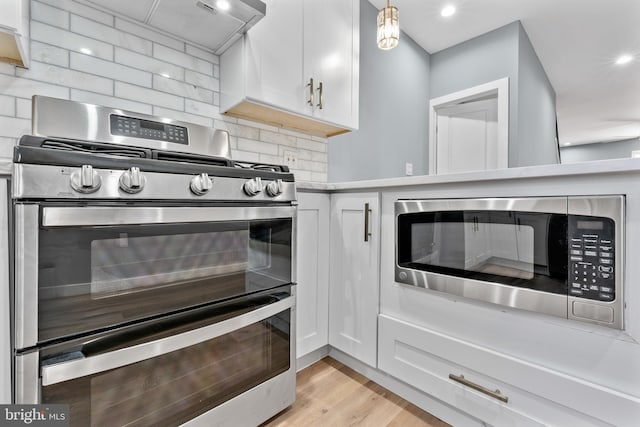 kitchen with light countertops, backsplash, white cabinetry, light wood-type flooring, and stainless steel appliances