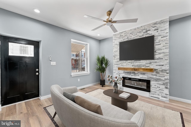 living room featuring a ceiling fan, baseboards, a fireplace, and wood finished floors