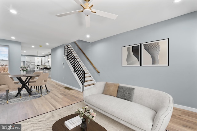 living room featuring stairway, light wood finished floors, baseboards, ceiling fan, and recessed lighting