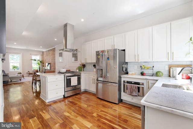 kitchen with a sink, light wood-style flooring, stainless steel appliances, white cabinetry, and island exhaust hood