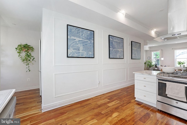 kitchen with stainless steel electric range oven, ventilation hood, light wood-style flooring, and white cabinetry