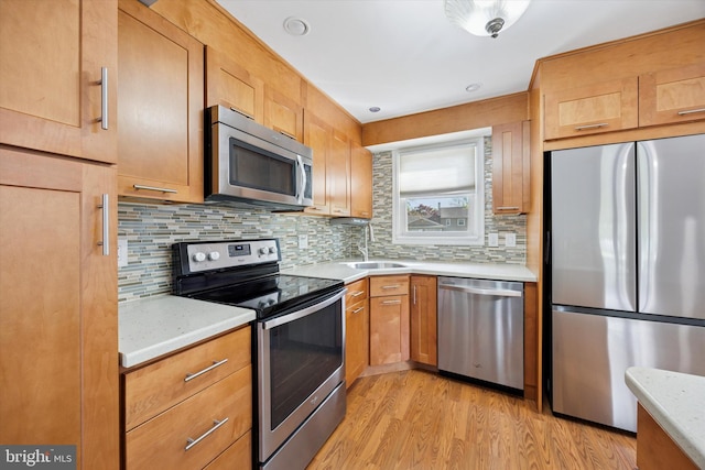 kitchen with light wood-style floors, light stone counters, a sink, backsplash, and stainless steel appliances
