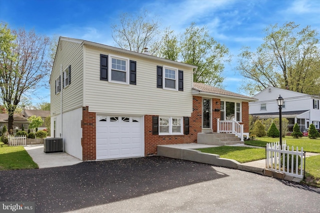tri-level home featuring fence, an attached garage, aphalt driveway, brick siding, and cooling unit