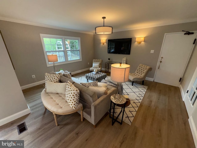 living room featuring baseboards, visible vents, crown molding, and wood finished floors