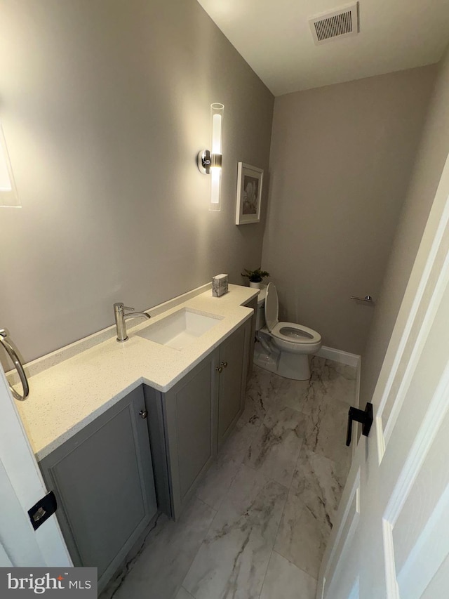 half bathroom with toilet, vanity, marble finish floor, baseboards, and visible vents