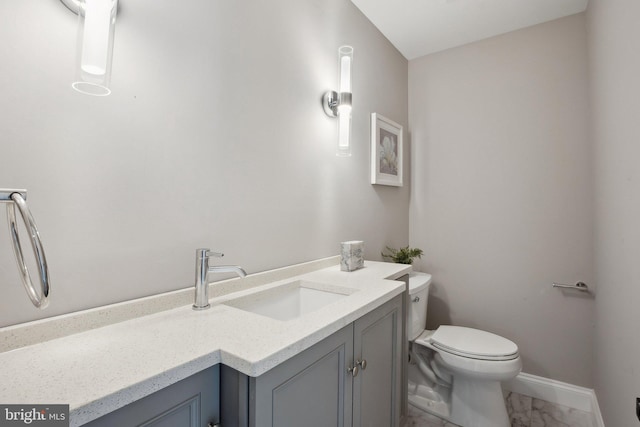 half bathroom with baseboards, marble finish floor, toilet, and vanity