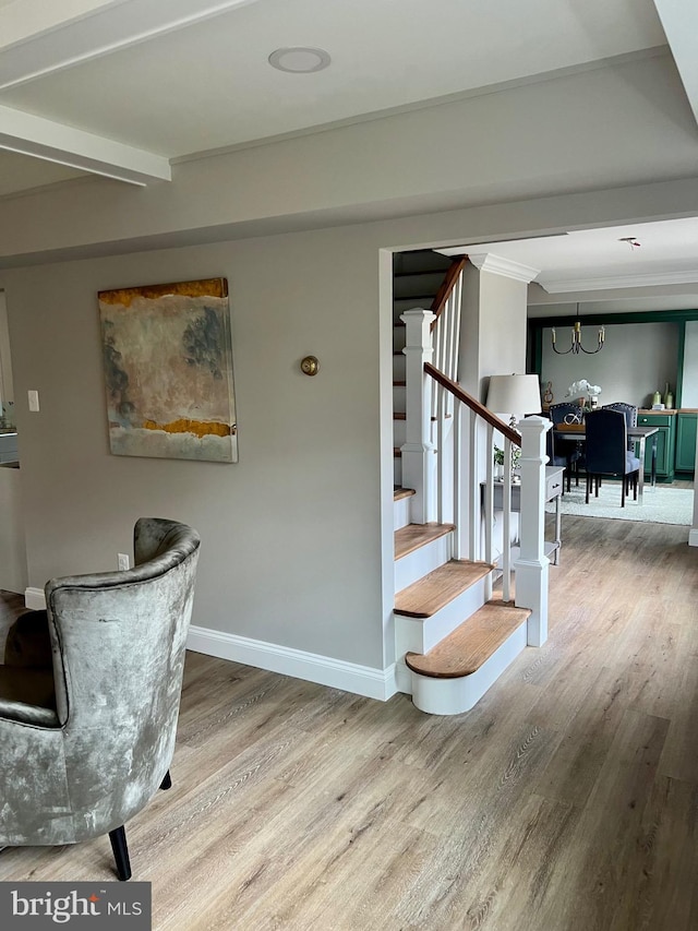 stairway with a notable chandelier, beam ceiling, baseboards, and wood finished floors