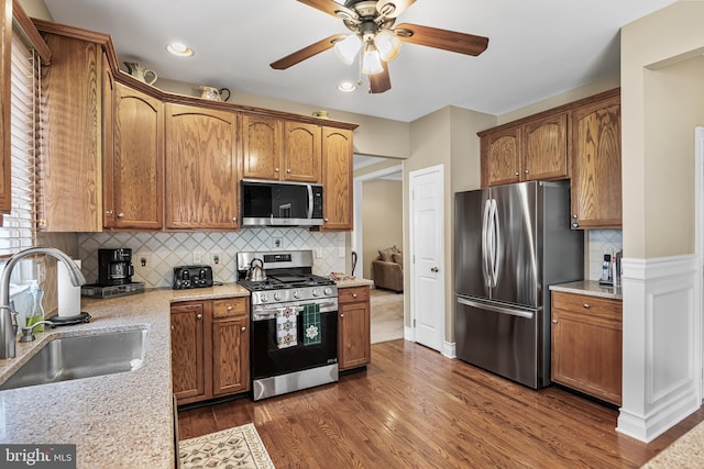 kitchen with a ceiling fan, appliances with stainless steel finishes, a sink, decorative backsplash, and dark wood-style floors