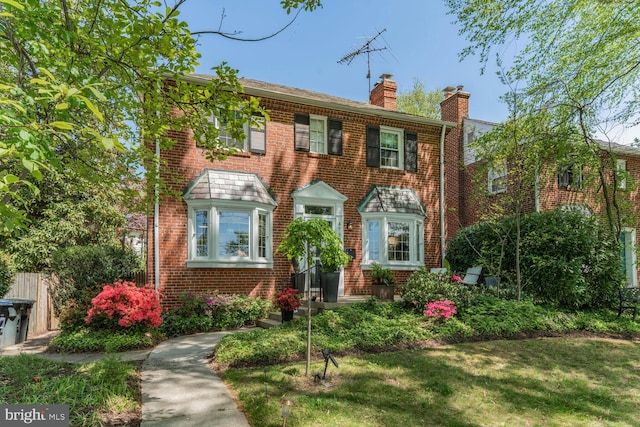 colonial-style house with a chimney, a front yard, and brick siding