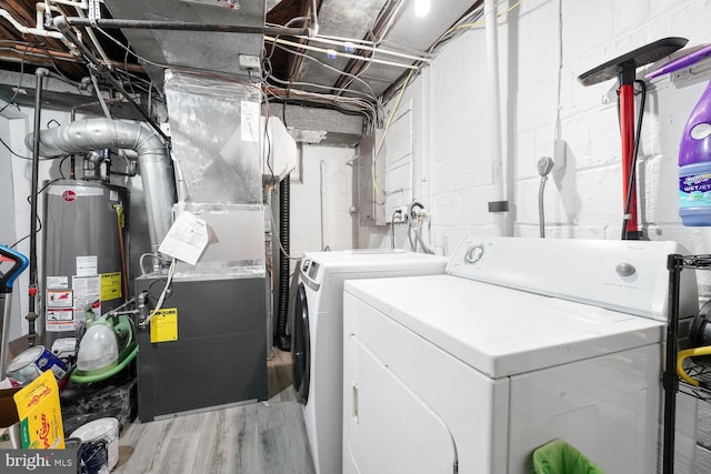 clothes washing area with laundry area, washing machine and dryer, wood finished floors, water heater, and heating unit