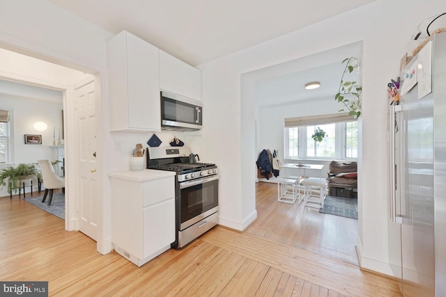 kitchen featuring appliances with stainless steel finishes, plenty of natural light, light wood-type flooring, and white cabinets