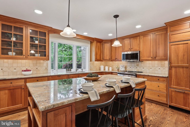 kitchen with appliances with stainless steel finishes, brown cabinetry, a sink, a kitchen island, and light wood-type flooring