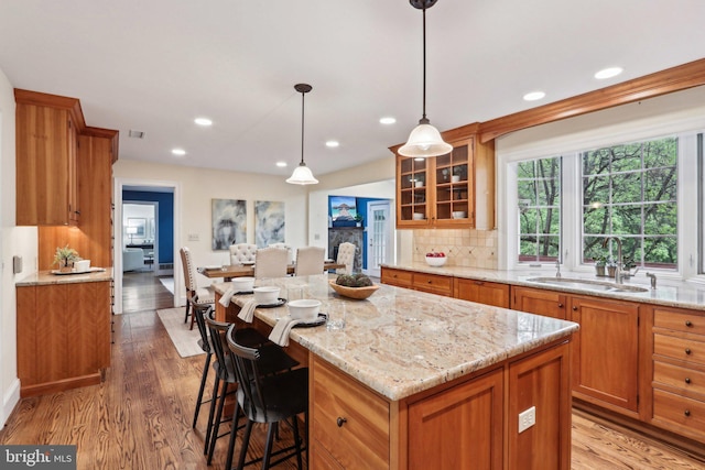 kitchen with a sink, brown cabinets, glass insert cabinets, light wood-style flooring, and light stone counters