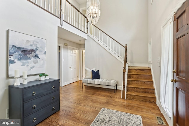 entryway featuring stairway, wood finished floors, baseboards, a high ceiling, and a chandelier