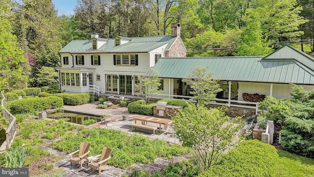 rear view of house with a chimney, a patio, a sunroom, metal roof, and a standing seam roof