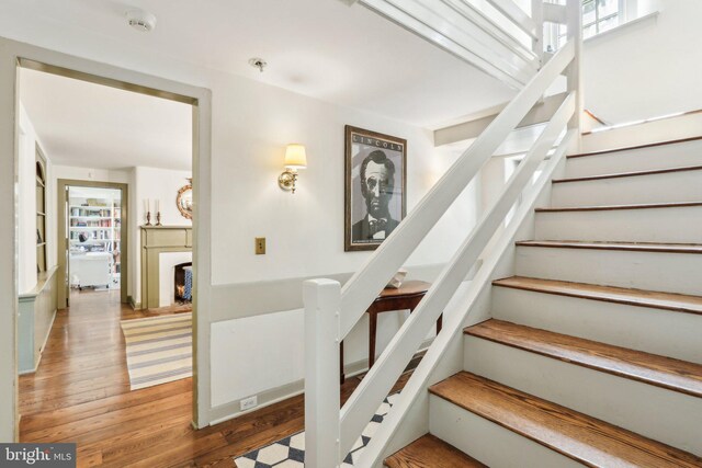 staircase featuring wood finished floors and a warm lit fireplace