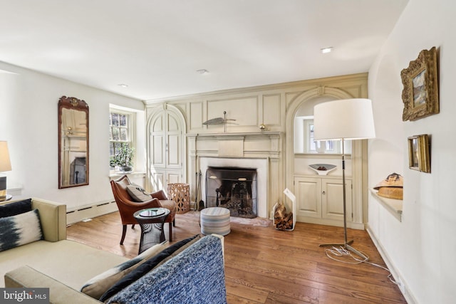 living room featuring a baseboard radiator, a fireplace with raised hearth, and light wood-style flooring