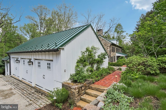 view of property exterior with board and batten siding, metal roof, an outbuilding, a chimney, and a standing seam roof