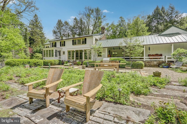rear view of property featuring a patio area, a chimney, and metal roof
