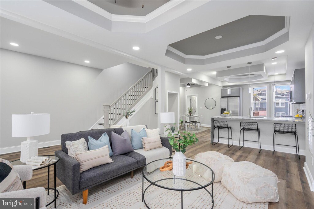 living area featuring baseboards, stairs, ornamental molding, wood finished floors, and a tray ceiling