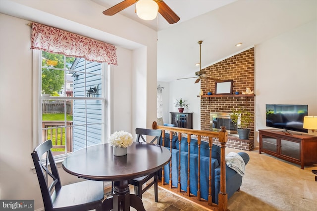 dining room featuring vaulted ceiling, a ceiling fan, carpet flooring, and a brick fireplace