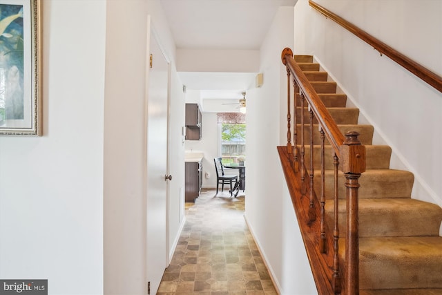 staircase with ceiling fan, stone finish flooring, and baseboards