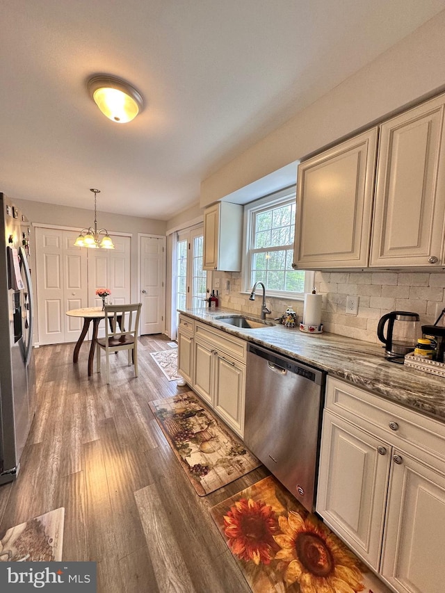 kitchen featuring wood finished floors, hanging light fixtures, appliances with stainless steel finishes, backsplash, and a sink