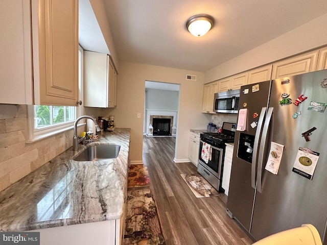 kitchen with light stone counters, stainless steel appliances, dark wood-style flooring, a sink, and visible vents