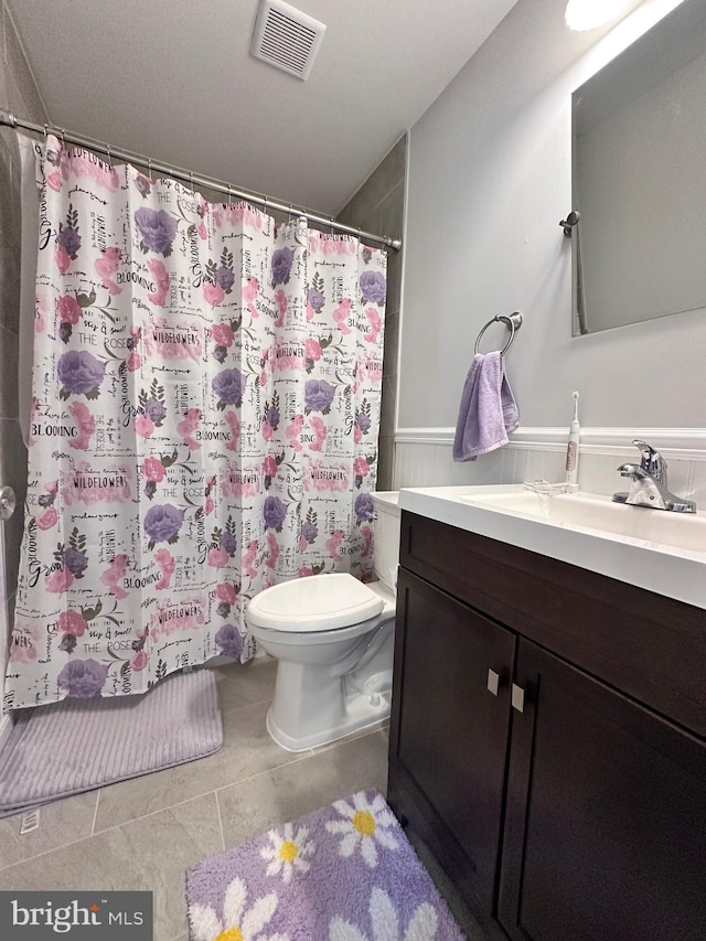 bathroom with tile patterned floors, a wainscoted wall, toilet, vanity, and visible vents
