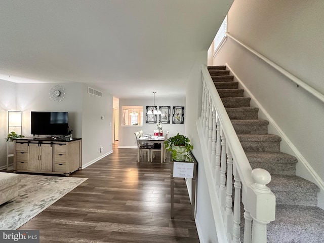 staircase featuring baseboards, visible vents, wood finished floors, and an inviting chandelier