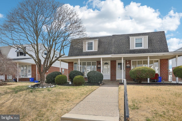 view of front of house featuring a front yard, a porch, brick siding, and roof with shingles