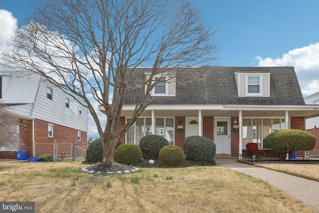 view of front of house with a shingled roof, a front lawn, covered porch, and brick siding