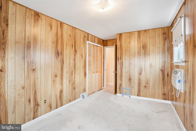carpeted empty room with heating unit, baseboards, visible vents, and wooden walls