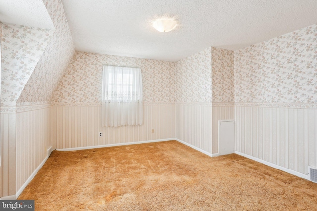 bonus room featuring wallpapered walls, a textured ceiling, carpet, and wainscoting