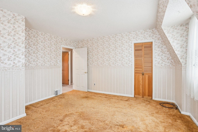 bonus room featuring a wainscoted wall, wallpapered walls, and a textured ceiling