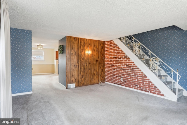 unfurnished living room featuring a textured ceiling, wallpapered walls, carpet, and an accent wall