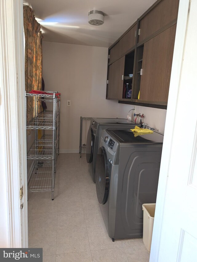 laundry area featuring baseboards, cabinet space, washer and clothes dryer, and light tile patterned floors
