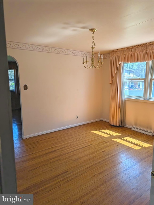 unfurnished dining area featuring arched walkways, baseboards, a chandelier, wood finished floors, and a baseboard radiator