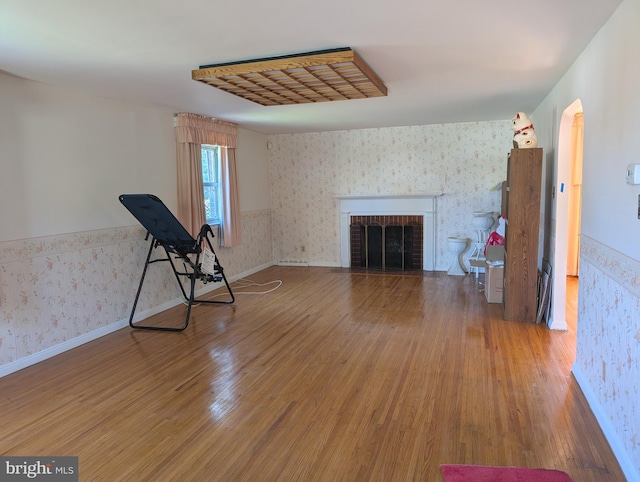 unfurnished living room featuring arched walkways, wood finished floors, wallpapered walls, and a fireplace
