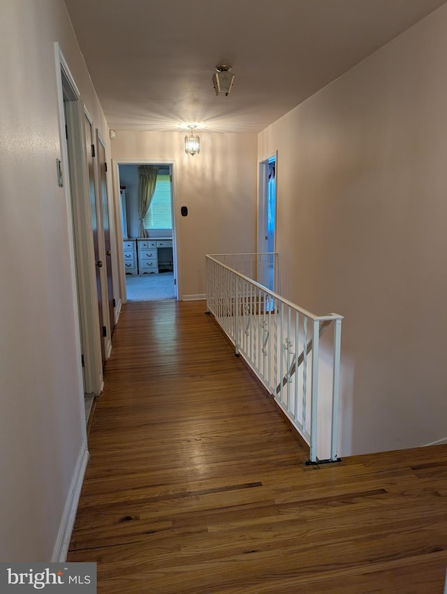 corridor featuring wood finished floors, baseboards, and an upstairs landing