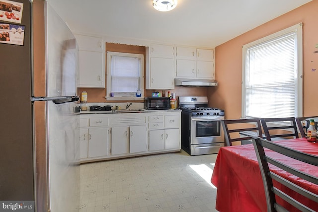 kitchen with light floors, white cabinetry, appliances with stainless steel finishes, under cabinet range hood, and a sink