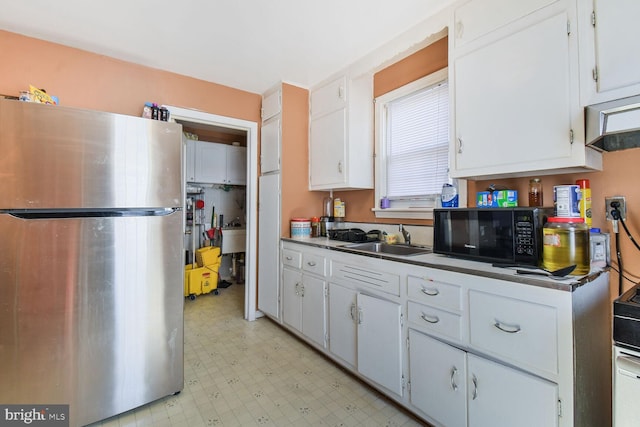 kitchen featuring freestanding refrigerator, light floors, black microwave, white cabinetry, and a sink