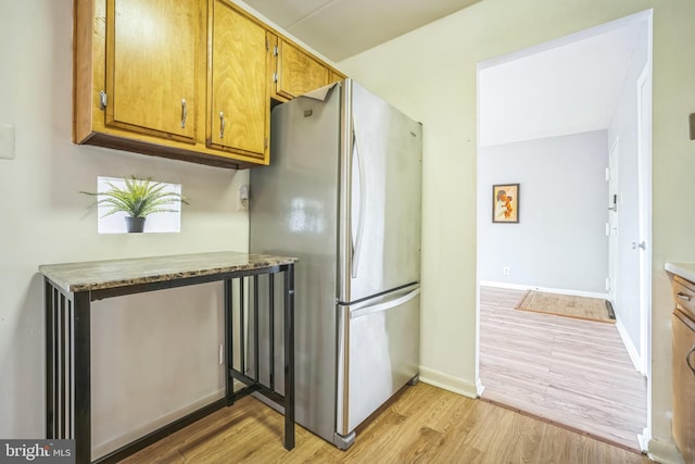 kitchen featuring freestanding refrigerator, baseboards, brown cabinetry, and light wood-style floors